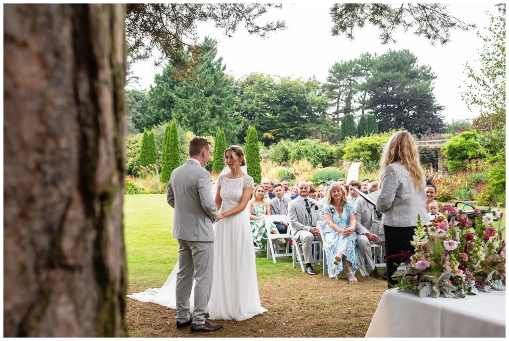 The bride and groom saying their vows in the grounds of Abbeywood Estate with their guests looking on